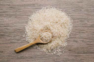 Ahşap arka planda tahta kaşıkta çiğ pirinç.