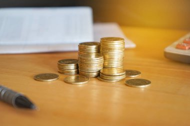 Hesap makinesi ve kalemle tahta bir masanın üzerindeki bozuk paralar.