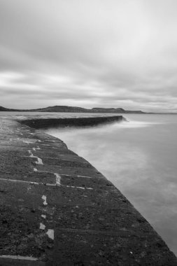 Long exposure of the tide washing up against the pier at Lyme Regis in Dorset clipart