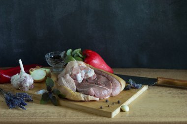 Kesme tahtasındaki çiğ domuz budu. Esmer arka planda otlar ve baharatlar var.