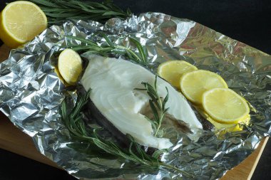 Siyah arka planda folyoda limonlu ve biberiyeli taze balık.