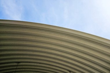 Kıvrımlı çelik kubbe çatısı, mavi gökyüzüne dokulu bir yüzeyi var..