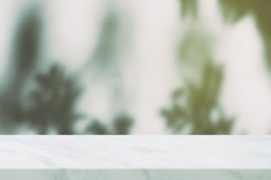 Önplanda beyaz mermer masa. Yeşil yaprakların bulanık arkaplanı ve ışık sızıntısı var..
