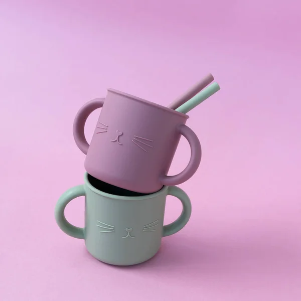 Modern pastel color silicone sippy cups with straws on pink background. Baby tableware, first feeding, serving concept
