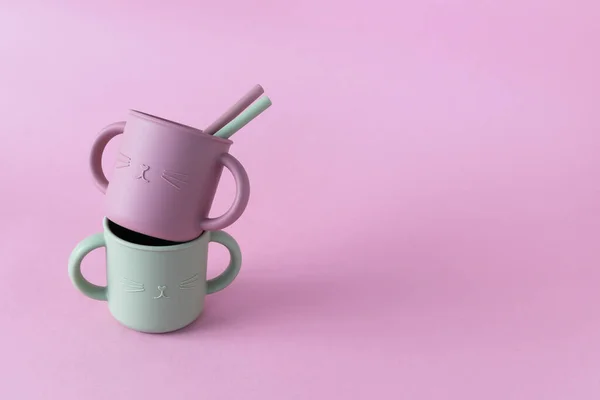 Modern pastel color silicone sippy cups with straws on pink background. Baby tableware, first feeding, serving concept.