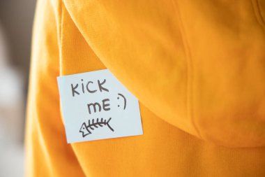 Sarı üzerine yapışkan bir kağıt ve KICK ME yazılı ve balık arkada, yakın plan. 1 Nisan Günü konsepti.
