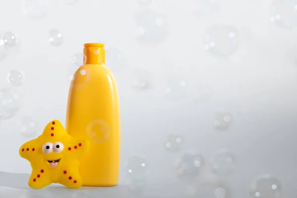 Baby bath foam or liquid soap with yellow star fish and many flying soap bubbles on white background. Childrens bath time concept. Copy space