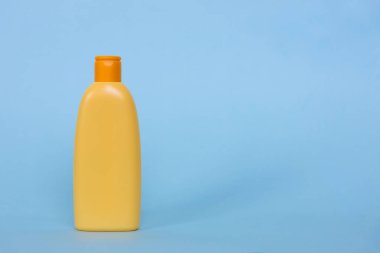Mavi zemin üzerinde kozmetik sıvısı olan sarı plastik bir şişeyi taklit et. Logo için boşluk.