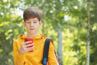 Sarı kapüşonlu genç, bahar zamanı açık havada cep telefonuna bakıyor.