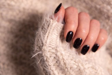 Beautiful female manicure of black color. Woman hand in cashmere knitwear. clipart