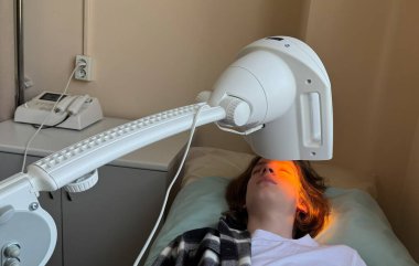 Göz hastalığını tedavi etmek için kızılötesi ısı tedavisi gören bir genç. Cihazların turuncu ışığı göz kapağını nazikçe ısıtır ve iyileşmesine yardımcı olur.