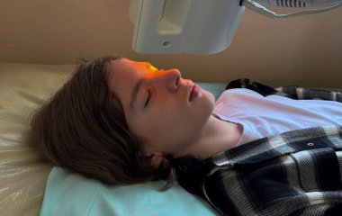 Chalazion tedavisi için kızılötesi terapi gören bir genç. Cihaz göz kapağı iltihabını azaltmak için sıcak turuncu ışık yayıyor.