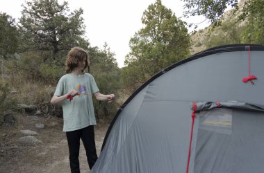 Kafkasyalı genç kampa giderken kamp malzemeleriyle gri çadır kuruyor. 