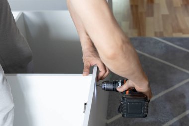 Evde elektrikli tornavidayla gardırop hazırlayan bir adam. Tahta panelleri bağlar, yapıyı güvene alır. Ev ortamında DIY mobilya montajı