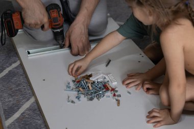Küçük kızları yardım ederken evde tornavidayla gardırop hazırlayan bir baba. Bir dakikalık aile çalışması ve ev dekorasyonu.