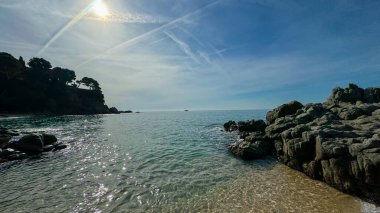 İspanya, Lloret de Mar 'daki sakin sahil manzarası. Yumuşak dalgalar açık bir gökyüzünün altında altın kumun üzerinde süzülüyor. Seyahat reklamları, arka planlar ve afişler için ideal