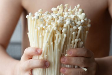 Çocuk usulca taze enoki mantarı tutuyor. Doğal gıda, merak, organik tarım ve sağlıklı beslenme kavramı.
