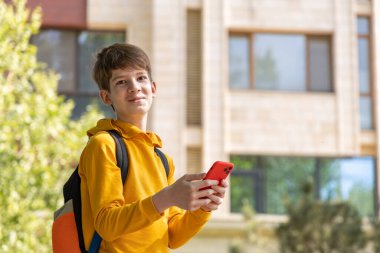 Akıllı telefon tutan gülümseyen genç çocuk, modern yeni evin önünde dikiliyor. Gençlik, teknoloji ve çağdaş banliyö yaşam tarzı konsepti.