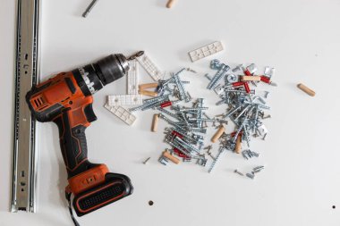 Beyaz yüzeyde çeşitli mobilya ve teçhizatla çevrili elektrikli tornavida. Ev yenileme, araçlar ve DIY montaj kavramı. 