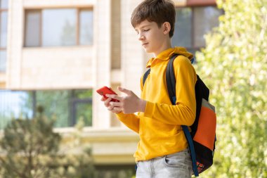 Ergen çocuk açık havada akıllı telefon kullanıyor, ekrana bakıyor, dijital çocukluğu ve modern teknolojiyi simgeliyor..