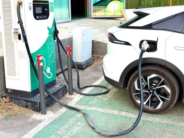 SHYMKENT, KAZAKHSTAN - 28 Eylül 2025: Şehir caddesindeki şarj istasyonuna bağlı modern beyaz elektrikli araba. Temiz enerji, eko taşımacılık ve sürdürülebilir teknoloji kavramı