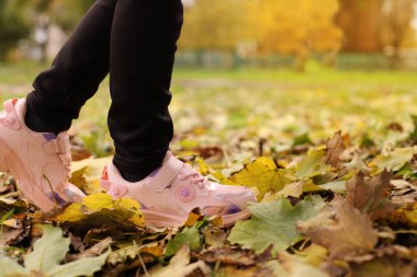 Kızın bacakları sonbahar yaprakları arasında yürür.