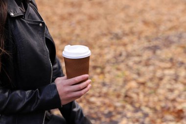 Sarı sonbahar yapraklarının arka planında bir bardak kahve tutan kız.