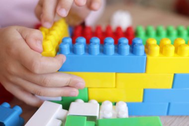 Çocuk masanın üstünde bir tasarımcıyla oynuyor, bloklardan duvarlar inşa ediyor.