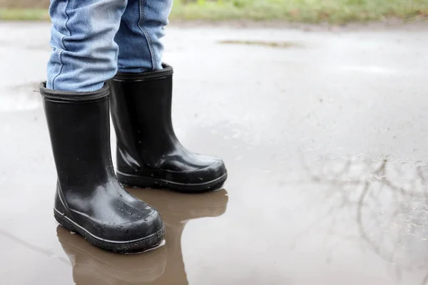 child in rubber boots in a puddle after rain
