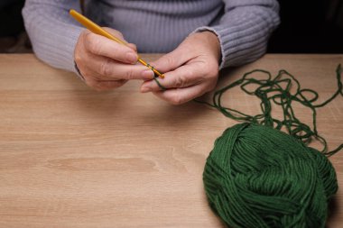 Kadının elleri, örgü örerek yün bir ürün örüyor. Ev yapımı kıyafet konsepti
