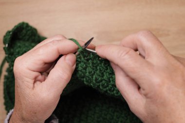 Kadın, masanın üstünde yün bir kazak örüyor.