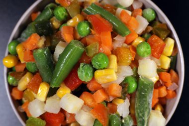 Mexican mix of frozen vegetable in a plastic bowl on a black background, top view