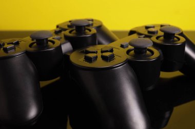 Wireless joystick gamepad controllers on a mirror surface on a yellow background