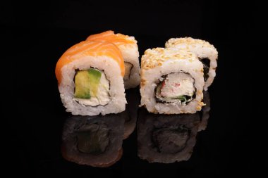 Various sushi with salmon, tuna, avocado, sesame on a mirror black surface