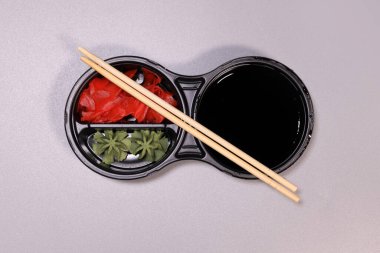 wasabi sauce, soy sauce and pickled ginger and chopsticks, a sushi set in a plastic container on a gray background