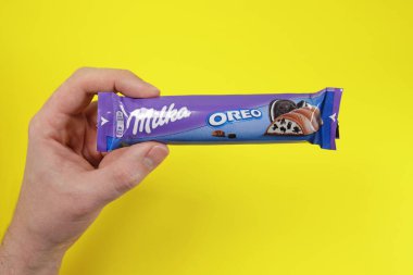 Magdalinovka, Ukraine - February 16, 2022. Milka alpine milk chocolate bar with Oreo cookie filling in hand on yellow background