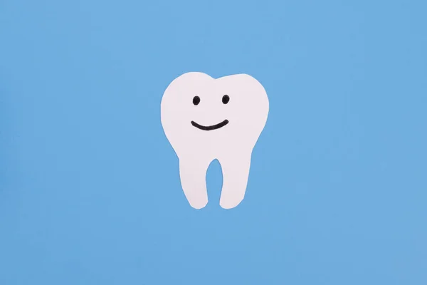White paper smiling tooth on a blue background. Dental treatment, dentist services, oral care
