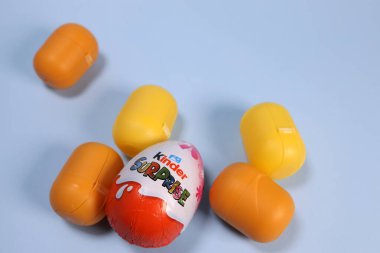 Magdalinovka, Ukrayna - 4 Mart 2023. Çikolata yumurtası Kinder sürprizi ve mavi arka planda oyuncağı olan bir kapsül.