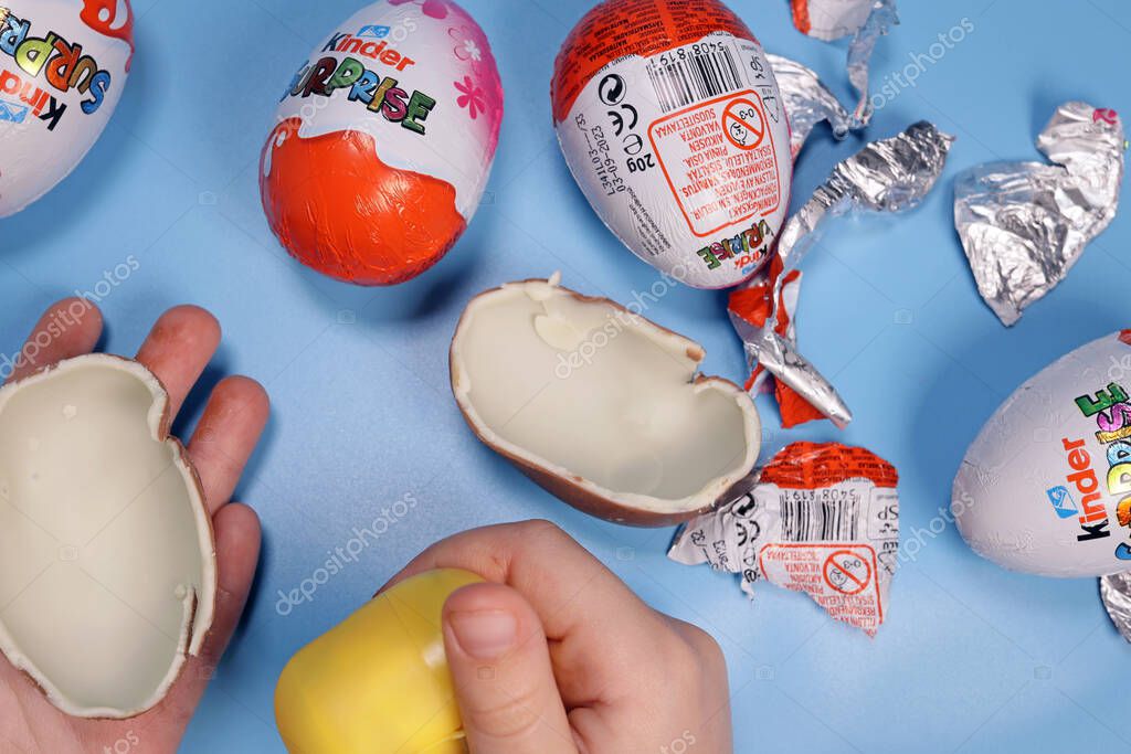 Magdalinovka, Ukraine - March 3, 2023. Child opens Kinder Surprise on a blue background