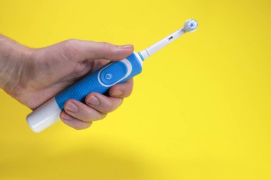 Sarı arka planda elektrikli diş fırçası, ağız temizliği kavramı