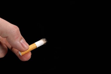 Smoldering cigarette, butt in hand on black background, smoking concept