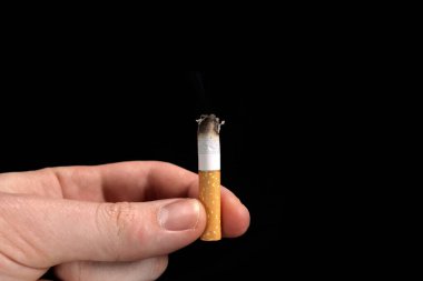 Smoldering cigarette, butt in hand on black background, smoking concept