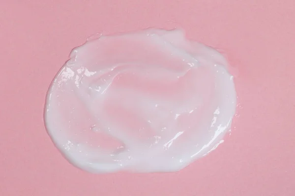 Smear of body or face cream on pink background, skin care concept