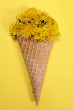 Sarı arka planda dondurmalı waffle külahında bir buket karahindiba çiçeği. Dikey Yönlendirme