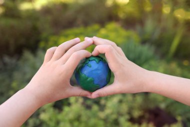 Yeşil bitkilerin arka planına karşı çocukların ellerinde plastik gezegen Dünya. Day Earth, çevre kavramını kaydet