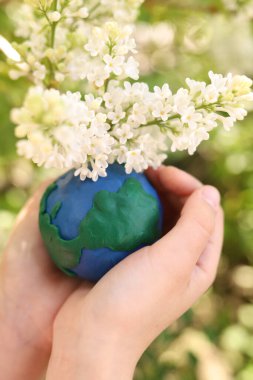 Çiçeklerin arkaplanındaki plastik gezegen Dünya çocukların ellerinde. Day Earth, çevre kavramını kaydet