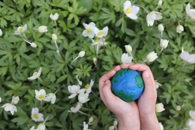 Çiçeklerin arkaplanındaki plastik gezegen Dünya çocukların ellerinde. Day Earth, çevre kavramını kaydet