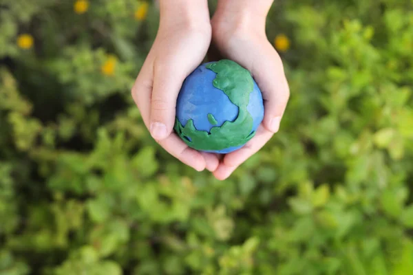 plasticine planet Earth in children\'s hands against the background of green plants. day earth, save environment concept
