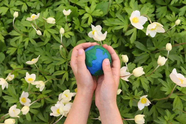 stock image child holds a plasticine planet Earth against a background of flowers. Concept day earth, save environment.