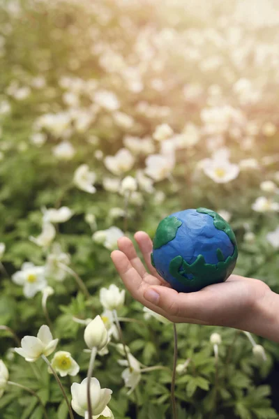 stock image plasticine planet Earth in children's hands on a background of flowers. day earth, save environment concept. Vertical Orientation